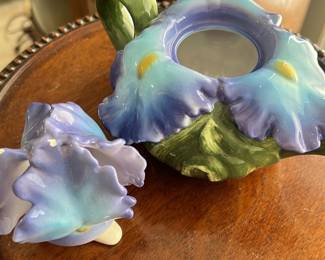 Purple Ceramic Iris Teapot — This charming ceramic teapot features a beautifully sculpted iris flower design with purple petals and green leaves. The piece is hand-painted and glazed with delicate gradients of violet, blue, and hints of yellow, reflecting a vintage floral style. It measures approximately 5.5 inches tall, 8 inches wide including the handle and spout, and 5.5 inches deep, making it an attractive decorative item or collectible teapot. The teapot shows no visible chips or cracks and is in good condition. Marked as made in the Philippines, it carries vintage appeal perfect for collectors or floral decor enthusiasts.