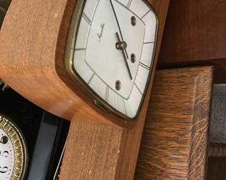 Mauthe Mid-Century Mantel Clock — This classic Mauthe mantel clock features a distinctive mid-century modern design with a wood case and brass accents. The clock face is white with an elegant geometric pattern and three winding holes, showcasing the brand's vintage German craftsmanship. Measuring approximately 6 in height, 10 in width, and 3 in length, it is a compact piece suitable for bedroom or living room decor. The clock is in good condition with some minor wear consistent with age and retains its original finish. A timeless collectible from the renowned Mauthe clockmakers, perfect for enthusiasts of vintage timepieces.