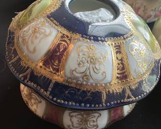 Decorative Hair Receiver Vase — This decorative hair receiver vase from the master bedroom features intricate patterns with gold accents on a rich cobalt blue and cream base. Designed as a two-piece ceramic with a wide opening on the lid, it combines both functionality and elegant design for vintage décor. Measuring approximately 4 in height and 5 in diameter, it is an ideal size for display or practical use. The vase is in good condition with minor surface wear consistent with age. A beautiful piece showcasing classic Victorian-style motifs, perfect for collectors or vintage enthusiasts.