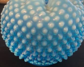 Blue Hobnail Milk Glass Vase — This charming blue hobnail milk glass vase features a striking ruffled edge and textured raised knobs around its rounded body. The vibrant blue color adds a vintage appeal, making it a perfect decorative accent for any room. It measures approximately 4 inches in height and 5 inches in width, ideal for small floral arrangements or as a stand-alone piece. The vase is in good condition with minor signs of wear typical for vintage glassware. Its classic hobnail design reflects mid-20th century glassmaking styles, perfect for collectors and enthusiasts.