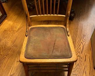 6-Carved Oak Dining Chairs — This vintage carved oak dining chair features a decorative scrolled top rail and a slat back design. Constructed from sturdy oak wood, it includes a worn brown seat cushion that adds rustic charm. Measuring approximately 39 inches in height, 18 inches in width, and 18 inches in depth, this chair is a perfect addition to a traditional dining room setting. The chair shows signs of wear on the cushion but remains structurally sound with no visible repairs. Its classic craftsmanship highlights a timeless style suitable for farmhouse or vintage decor.
