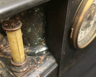 Antique Black Resin Mantel Clock — This antique black mantel clock features elegant brass detailing and ornate columns with a classic design. The clock face displays bold black numerals around a gold embossed center, enclosed in a brass bezel. Measuring approximately 12 inches tall, 16 inches wide, and 6 inches deep, it is a substantial piece ideal for display on a mantel or shelf. The clock shows some wear consistent with age, including minor chipping and surface scratches, but remains a charming vintage collectible. Its Victorian-era styling and craftsmanship make it a distinctive addition for antique enthusiasts.