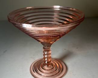 Vintage Pink Depression Glass Compote — This vintage pink depression glass compote features a distinctive ribbed design with concentric circles on the bowl and the base. The elegant pedestal stem is crafted to complement the overall ribbed pattern, showcasing authentic depression-era glasswork. Measuring approximately 4.25 inches in height and 5.5 inches in diameter, this compote is perfect for display or serving small treats. The piece is in very good vintage condition with no visible chips or cracks, retaining its original pink color and clarity. A charming example of Depression-era collectible glassware, ideal for collectors and vintage decor enthusiasts.