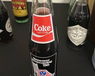 Coke Tennessee Homecoming '86 Bottle — This vintage Coke glass bottle commemorates the Tennessee Homecoming event from 1986. Featuring a classic red Coke logo on the neck and a special event label on the body, it is a collectible piece for soda enthusiasts. The bottle holds 10 fluid ounces, stands approximately 7.5 inches tall, and is made with traditional glass. It is in very good condition with original contents and unopened. A nostalgic collectible that represents a significant regional event from the mid-1980s.