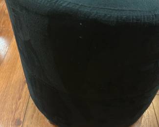 Black Velvet Round Ottoman — This black velvet round ottoman offers a plush and versatile seating or footrest option. It features a smooth, soft velvet upholstery with a central button tuft for subtle detailing. The ottoman measures approximately 18 inches in height and 16 inches in diameter, making it compact and easy to place in any living space. In good condition with minor signs of wear consistent with light use. Its simple cylindrical design complements various decor styles, ideal for basement or living room settings.