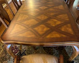 Dining Room Wood Inlaid Table & chairs — This elegant dining room table features a finely crafted wood surface with intricate inlaid diamond patterns. The table is supported by sturdy cabriole legs and comes with matching upholstered armchairs in a beige diamond pattern fabric. Measuring approximately 31 inches in height, 42 inches in width, and 90 inches in length, it offers ample seating for family and guests. The piece is in good condition with minor surface scratches consistent with normal use. Its classic design and quality woodwork make it a versatile addition to any traditional dining space.
