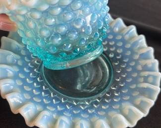 Fenton Blue Opalescent Hobnail Bowl Set — This charming Fenton blue opalescent hobnail bowl set features a delicate ruffled edge and the signature hobnail texture. Crafted in vintage art glass, the bowl nestles into a matching plate, both radiating an iridescent blue color with a milky white opalescent rim. The bowl measures approximately 3.5 inches tall with a 4.5-inch diameter, and the plate is about 6.5 inches wide. Both pieces are in excellent vintage condition without chips or cracks, showcasing Fenton's renowned craftsmanship. A lovely collectible for vintage glassware enthusiasts.