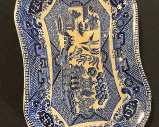 Semi-Vitreous Blue Willow Dish — This charming semi-vitreous dish features the iconic Blue Willow pattern in classic blue and white. Crafted from ceramic with a semi-vitreous finish, it displays traditional Chinese-inspired motifs including pagodas, bridges, and willow trees framed by a decorative patterned border. Measuring approximately 11.5 inches in length and 7.5 inches in width, it is a versatile serving or decorative piece. The dish is in good condition with minor surface wear and some glaze imperfections typical of vintage ceramics. The maker's mark on the bottom confirms its semi-vitreous composition and adds to its collectible appeal.