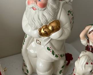 Lenox Santa Skates Cookie Jar — This charming Lenox Holiday white Santa cookie jar features detailed holly and gift motifs with gold accent mittens and hat pom-pom. Crafted from fine porcelain, it depicts Santa carrying a sack filled with toys including a teddy bear and clown. Measuring approximately 12 inches tall, this festive collector's piece adds a traditional holiday touch to any kitchen or display. The jar is in excellent condition with no visible chips or cracks, maintaining its bright and glossy finish. Made in 1999 by Lenox, this piece reflects the brand's long-standing reputation for quality holiday ceramics.