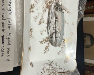 CFH Gold Trim Winter Scene platter — This elegant CFH rectangular platter features gold vines and leaves decorating its scalloped edges, with a central oval winter scene depicting a cabin and bird. The platter combines fine porcelain craftsmanship with delicate gilded accents, making it a beautiful decorative or serving piece. Measuring approximately 14 inches wide by 8 inches long and 1.5 inches tall, it is ideal for display or special occasions. The platter is in good condition with minor age-appropriate wear on the gilding, retaining its charm and collectible appeal. Marked CFH GDM on the bottom, it reflects quality maker's mark identification.