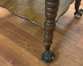 Oak End Table with Claw Feet — This charming oak end table features a scalloped top and a lower shelf for added storage or display. The table is supported by intricately turned legs ending in distinctive claw feet, adding a vintage touch. Measuring approximately 26 inches high, 28 inches wide, and 20 inches deep, it fits well in various living spaces. The piece is in good condition with minor surface wear consistent with age, preserving its character and sturdy construction. Ideal for use as a side table or accent piece in traditional or rustic decor.