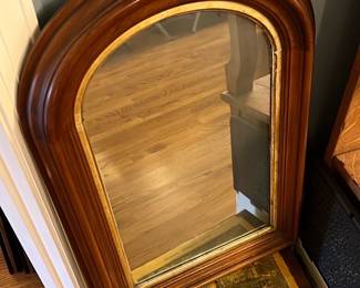 Arched Wood Frame Wall Mirror — This elegant arched wall mirror features a richly finished wooden frame with a smooth rounded profile. The mirror glass is bordered by a subtle gold inner trim that adds a classic touch to its design. Measuring approximately 34 inches tall and 22 inches wide, the piece offers a versatile size ideal for living room decor. It is in good condition with minor wear to the frame consistent with age and use but no visible damage to the glass. This mirror complements traditional and vintage-inspired interiors with its warm wood tones and graceful shape.