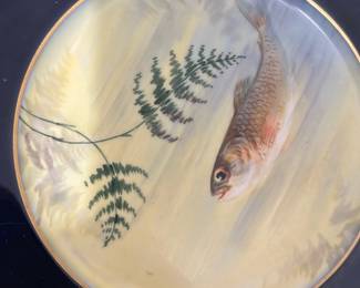 10Limoges France Blue Fish Plates Set — This set of 10 Limoges France plates features a distinctive dark blue border with gold trim and a detailed hand-painted fish design in the center. Crafted from fine porcelain, these collectible plates combine traditional artistry with elegant decoration, making them perfect for decorative or functional use. Each plate measures approximately 10.5 inches in diameter, ideal for display or serving. The plates are in good condition with no visible chips or cracks, showcasing their enduring quality. A beautiful example of Limoges craftsmanship, these plates add a classic touch to any collection or dining setting.