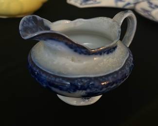 Waldorf Blue Creamer Pitcher — This Waldorf blue and white ceramic creamer pitcher is a charming addition to any vintage kitchen collection. Featuring a delicate, scalloped rim and a classic blue floral design on white glazed pottery, this piece is both decorative and functional. The pitcher stands approximately 3.5 inches tall with a width of 5 inches from spout to handle, and has a sturdy construction typical of historic English pottery. It is in good condition with some minor surface wear consistent with its age. Marked on the bottom with 'Waldorf England Ware'.