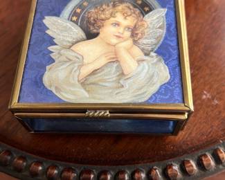 Via Vermont Angel Glass Jewelry Box — This handcrafted Via Vermont glass jewelry box features a charming angel motif on the lid, set against a blue background. Made in Mexico, it includes mirrored interior and exterior panels with a brass frame and decorative feet. The box measures approximately 4.5 inches in height, width, and length, making it a perfect compact storage piece. It is in excellent condition with minimal wear and retains the original maker's label and artwork attribution to Thomas Gatley (1993). A beautiful decorative and functional collectible for any jewelry lover.
