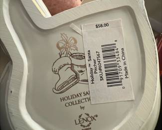 Lenox Holiday Santa Pitcher — This charming Lenox Holiday Santa Pitcher is a delightful addition to any Christmas decor collection. Crafted from fine porcelain, it features a classic white finish accented with green holly leaves, red berries, and shiny gold details on the mittens and bell. Measuring approximately 7 inches tall, this piece combines festive appeal with practical function. It is in excellent condition with no visible chips or cracks, retaining its original glossy finish. Part of the Holiday Santa Collection by Lenox, it captures the timeless spirit of the season.