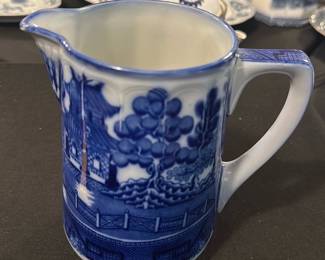 Doulton Burslem England Willow Pitcher — This charming Doulton Burslem England pitcher features the iconic blue Willow pattern, celebrated for its intricate and traditional design. Crafted from fine porcelain, this piece displays detailed scenic motifs with a classic spout and handle. The pitcher measures approximately 4.5 inches in height and 3.5 inches in width, making it a perfect addition to any blue dishes collection. It is in good condition with minor age-related wear on the base but no chips or cracks. A certified piece from the renowned Doulton factory, it embodies classic English ceramic artistry.