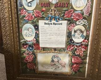 God Bless Our Baby Framed Record — Charming framed "God Bless Our Baby" baby record with colorful Victorian-style illustrations and floral borders. The piece features a printed baby's record center with spaces filled in by hand and is set in an ornate gold-toned molded frame. Frame measures approximately 24 inches high by 18 inches wide and is a lightweight decorative piece suitable for nursery or wall display. Condition is good for age with light wear to frame gilt and minor foxing/toning to the paper; glass appears intact.