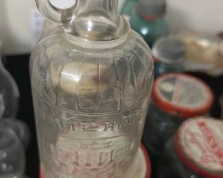 Vintage White House Jar — This vintage White House honey jar features clear glass with embossed branding and a pouring spout. It has a distinctive rounded body with vertical ridges and a loop handle near the spout for easy pouring. Measuring approximately 8 inches in height and 3.5 inches in diameter, this jar offers a charming way to serve honey or syrup. The jar is in good condition with some expected wear and minor surface marks consistent with age. A unique collectible piece ideal for kitchen decor or as a vintage serving vessel.