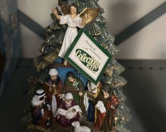 Collectibles Elite musical Nativity Tree — This Collectibles Elite ceramic Christmas tree features a detailed nativity scene at the base with an angel topper and gold star. Painted in green, white and gold tones with hand-painted detailing, the piece appears to be a plug-in or battery-powered lighted decoration (base shows electronics). Measures approximately 12 inches tall and is a sturdy tabletop holiday accent. Good estate-sale condition with minor surface wear consistent with display; electronics untested but base appears intact. Ideal for holiday décor or collectors of seasonal ceramics from the Collectibles Elite line.
