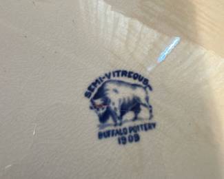 Blue Willow Platter — This vintage Buffalo Pottery blue willow platter dated 1909 features a classic semi-vitrous ceramic construction with intricate blue scenic patterns typical of the willow design. The platter measures approximately 12 inches wide and 15.5 inches long, making it a versatile serving dish or decorative piece. It displays a lovely crackle glaze consistent with its age but remains in good condition with no visible chips or cracks. The iconic buffalo logo and date stamp confirm its authenticity and add historical value to this collectible pottery piece.