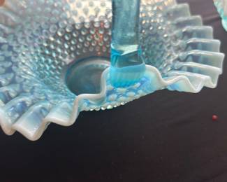 Fenton Blue Opalescent Hobnail Basket — This exquisite Fenton blue opalescent hobnail glass basket features a striking ruffled edge and a sturdy curved handle, typical of Fenton's classic design. The opalescent blue glass with hobnail texture catches light beautifully, making it a stunning decorative and collectible piece. Measuring approximately 9 inches in height, 9 inches in width, and 6 inches in length, it is ideal for display or functional use. The basket is in excellent condition with no chips, cracks, or repairs visible, reflecting careful preservation. As a vintage collectible from the renowned Fenton Art Glass Company, it represents fine American craftsmanship in art glass.