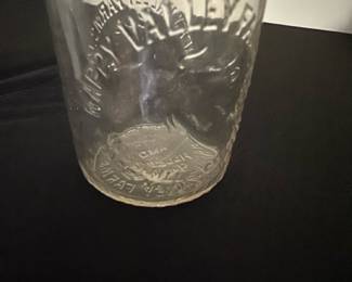 Happy valley Dairy Clear Glass Milk Bot — This vintage Crowley Farm Dairy milk bottle features clear glass embossed with a farm scene including a cow and lettering. The bottle has a narrow neck with a rounded lip and stands as a collectible piece of dairy history. It measures approximately 8.25 inches tall and 3.25 inches wide, making it a classic size for milk bottles from the mid-20th century. The item is in good condition with some wear consistent with age, including minor cloudiness and light surface marks but no chips or cracks. This piece represents a charming relic of traditional dairy farming, perfect for collectors or rustic decor enthusiasts.
