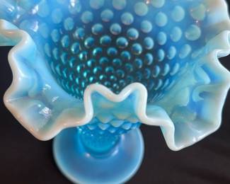 Blue Hobnail Ruffled Edge Vase — This striking blue hobnail glass vase features a distinctive ruffled edge with an opalescent finish that highlights its exquisite craftsmanship. The textured hobnail pattern adds elegance and tactile interest to this decorative piece. Measuring approximately 9 in height and 6 in across the widest ruffled opening, it serves as a beautiful accent for any master bedroom décor. The vase is in excellent condition with no chips, cracks, or damage observed. Its vintage style makes it perfect for collectors or as a statement home décor item.