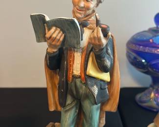 Ardco Fine Quality Porcelain Figure — This charming Ardco Fine Quality porcelain figurine from Dallas depicts a cheerful man reading a book while holding a pipe. Crafted in Japan, this finely detailed piece features hand-painted colors including teal, brown, and cream tones. The figurine measures approximately 10 inches tall, ideal for display on a shelf or mantel. It is in good condition with minor surface wear consistent with age and no visible chips or cracks. A delightful collectible that reflects mid-century craftsmanship and artistry.