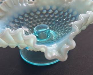 Fenton Blue Opalescent Hobnail Candlehol — This charming Fenton blue opalescent hobnail candleholder features a ruffled edge with a hobnail pattern on the bowl and a sturdy pedestal base. The blue glass with opaline white edge adds a delicate vintage look perfect for decorative settings. Measuring approximately 4.5 inches in height and 7 inches in diameter, it is a versatile accent piece for any room. The candleholder is in good vintage condition with slight wear consistent with age and use. A classic collectible from Fenton, this piece showcases the brand's signature artistry and glass craftsmanship.