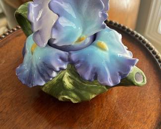 Purple Ceramic Iris Teapot — This charming ceramic teapot features a beautifully sculpted iris flower design with purple petals and green leaves. The piece is hand-painted and glazed with delicate gradients of violet, blue, and hints of yellow, reflecting a vintage floral style. It measures approximately 5.5 inches tall, 8 inches wide including the handle and spout, and 5.5 inches deep, making it an attractive decorative item or collectible teapot. The teapot shows no visible chips or cracks and is in good condition. Marked as made in the Philippines, it carries vintage appeal perfect for collectors or floral decor enthusiasts.