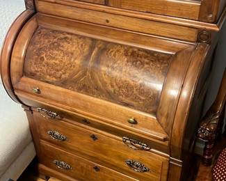 Wood Roll-Top Secretary Desk — Attractive wooden roll-top secretary desk with glass-front upper cabinet and brass hardware; perfect for a master bedroom or home office. Constructed of medium-tone hardwood with a burled roll-top, three lower drawers with decorative brass pulls, and an upper display cabinet with two glass doors and interior shelving. Overall footprint is medium-sized and practical for writing and storage; roll-top opens to reveal small cubbies and drawers for organization. Good estate-sale condition with light surface wear and patina consistent with normal use, hardware intact and drawer function smooth.