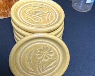 8 Vintage Yellow Pottery Coasters Set — This set of vintage yellow pottery coasters features a charming embossed floral and abstract design. Crafted from ceramic with a warm speckled yellow glaze, each coaster adds rustic charm while protecting surfaces. The coasters measure approximately 4 inches in diameter, offering a practical size for most drinkware. They are in good condition with minor wear consistent with age, adding character without compromising function. Ideal for collectors or for adding a vintage touch to any home décor.