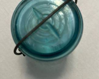 Ball Aqua Glass Jar with Wire Bale — This vintage Ball glass jar features a distinctive aqua blue color and a wire bale closure, typical of early 20th-century canning jars. Made from thick glass, it includes embossed Ball branding and a patent date indicating its collectible nature. Measuring approximately 4 inches in height and 3 inches in diameter, it is a sturdy piece suitable for display or storage. The jar is in good condition with signs of use and some minor wear to the wire bale closure. A great addition for collectors of vintage kitchenware or rustic home decor.