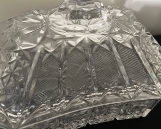 Pressed Glass Covered Candy Dish — This elegant pressed glass covered candy dish features intricate diamond and fan patterns that catch the light beautifully. The lid boasts a tall faceted handle for easy lifting, complementing the geometric design. Measuring approximately 5.5 inches high, 7.5 inches wide, and 5 inches deep, this piece adds a classic touch to any bedroom or dining room display. The dish is in good condition with no visible chips or cracks, preserving its vintage appeal. Ideal for holding candies, small treats, or trinkets, it enhances both functionality and style.