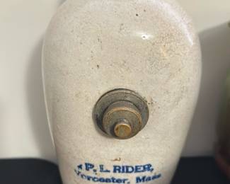 P.L. Rider Hendersons Foot Warmer — This vintage P.L. Rider foot warmer from Worcester, Massachusetts, showcases classic stoneware craftsmanship with a crackled cream glaze. Featuring a functional brass knob on its front, this Hendersons model is a practical and collectible piece of Americana. The item stands approximately 9 inches tall and 5 inches wide, making it suitable for personal use during cold weather. It shows typical age wear and surface crackling, consistent with its vintage origin, but remains structurally sound. A wonderful addition for collectors of antique home warming devices and stoneware.