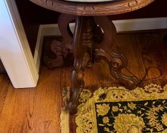 Victorian Marble Top Side Table — This Victorian marble top side table features a solid wood base with intricately carved legs and rim details, supporting a thick round white marble top with gray veining. The craftsmanship highlights a classic 19th-century style, combining robust wood construction with elegant stone. The table measures approximately 28 inches in height and 24 inches in diameter, making it an ideal accent piece for any front room. It is in good condition with minor surface wear consistent with age but no visible structural damage or cracks in the marble. This table adds a touch of antique charm and functional style to your home décor.
