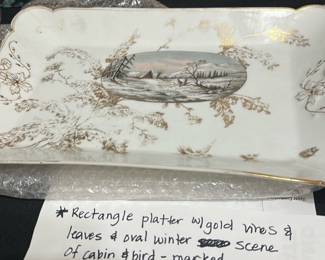 CFH Gold Trim Winter Scene platter — This elegant CFH rectangular platter features gold vines and leaves decorating its scalloped edges, with a central oval winter scene depicting a cabin and bird. The platter combines fine porcelain craftsmanship with delicate gilded accents, making it a beautiful decorative or serving piece. Measuring approximately 14 inches wide by 8 inches long and 1.5 inches tall, it is ideal for display or special occasions. The platter is in good condition with minor age-appropriate wear on the gilding, retaining its charm and collectible appeal. Marked CFH GDM on the bottom, it reflects quality maker's mark identification.