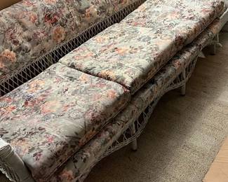 Vintage Floral Wicker Sofa 77” Long — This vintage wicker sofa features a delicately woven frame with a classic floral cushioned upholstery that adds a quaint charm. The cushions showcase a muted color palette of soft apricot, rose, and gray floral patterns, enhancing its traditional aesthetic. Measuring approximately 72 inches wide, 30 inches deep, and 28 inches tall, it fits well in cozy living areas or sunrooms. The piece is in good condition with some expected wear on the cushions and minor signs of aging on the wicker frame, typical for a vintage item. This sofa embodies timeless craftsmanship ideal for casual and vintage-inspired decor.