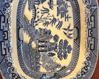 Blue Willow Semi-Vitreous Platter — This semi-vitreous blue willow platter features the classic blue and white transferware pattern with pagodas, trees, and birds. The platter measures approximately 12.5 inches in width and 10 inches in height, making it a versatile serving piece or decorative item. It shows signs of crazing consistent with age but remains structurally sound without visible chips or cracks. Ideal for collectors of vintage blue and white china, this platter adds a timeless touch to any table setting or display.