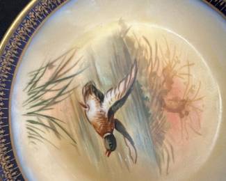 Limoges Hand-Painted Duck bowl — This beautiful Limoges plate features a hand-painted mallard duck in flight over a serene water scene. The plate has a deep blue and gold decorative border that enhances its classic elegance. Measuring approximately 10 inches in diameter, it is marked on the back with 'Limoges, France' and 'Lambides R&Co Paris.' The plate is in good condition with minor surface wear consistent with age and use. A stunning collectible from the renowned Limoges porcelain makers, perfect for display in any bedroom or dining collection.