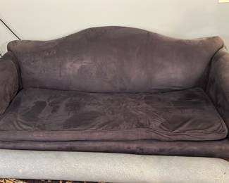 Dark Blue Upholstered Sofa — This dark blue upholstered sofa features a gently curved back and rolled arms with wood trim detailing on the armrests. The plush seat cushion provides comfortable seating, making it a cozy option for living room use. The sofa measures approximately 36 inches in height, 84 inches in width, and 35 inches in depth, making it suitable for medium to large spaces. It is in good condition with some visible cushion wear and minor fabric impressions but no major damage. The design has a traditional feel, complemented by the wooden accents.