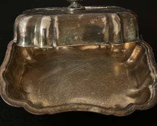 Vintage Silver plated Butter Dish — This vintage silver-plated butter dish features an elegant curved lid with a decorative finial handle. The tray has a scalloped edge and a polished interior, perfect for serving butter or small delicacies. Measuring approximately 3 inches high, 7 inches wide, and 5 inches deep, it is compact and functional for any table setting. The dish shows light tarnish and surface wear consistent with age but remains in good condition overall. A charming addition to vintage tableware collections or antique decor.