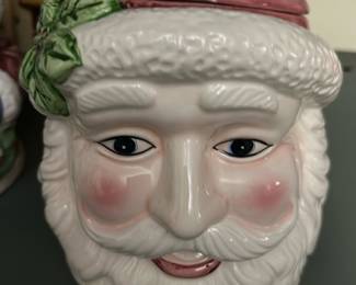 Ceramic Santa Cookie Jar — Charming ceramic Santa cookie jar with a removable hat lid, displayed in the blue dishes room. Hand-painted face with rosy cheeks, molded beard detail and holly accent on the hat; glazed finish shows light paint wear at the lid rim. Overall size is compact and countertop-friendly; holds a modest batch of cookies or candy. Good estate-condition with no obvious large chips or cracks visible in photos, minor rim paint loss noted.