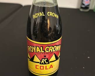 Royal Crown Cola Vintage Glass Bottle — This vintage Royal Crown Cola glass bottle features classic branding with a red and yellow label and the iconic RC logo. The bottle has the traditional shape of mid-20th century soda bottles, complete with a metal cap and embossed lettering on the neck. Measuring approximately 7.5 inches tall, it is a collectible item perfect for soda enthusiasts or vintage collectors. The bottle is in good condition with minimal wear visible on the label and no apparent cracks or chips. A great nostalgic piece representing American soda history.