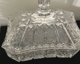 Pressed Glass Covered Candy Dish — This elegant pressed glass covered candy dish features intricate diamond and fan patterns that catch the light beautifully. The lid boasts a tall faceted handle for easy lifting, complementing the geometric design. Measuring approximately 5.5 inches high, 7.5 inches wide, and 5 inches deep, this piece adds a classic touch to any bedroom or dining room display. The dish is in good condition with no visible chips or cracks, preserving its vintage appeal. Ideal for holding candies, small treats, or trinkets, it enhances both functionality and style.