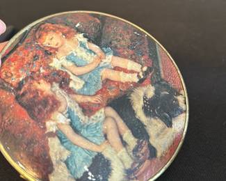 Vintage Double-Sided Round Compact Mirro — This vintage double-sided round compact mirror features a charming printed image of two girls in blue dresses with a dog, capturing a nostalgic scene on the exterior. The compact is crafted from metal with a brass tone finish, offering two functional mirrors within its hinged design. Measuring approximately 3.5 inches in diameter, it is a delicate and portable accessory suitable for personal use or display. The item shows signs of wear on the printed image but remains structurally intact and fully functional. Ideal as a collectible or a vintage beauty accessory.