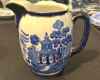 Buffalo Pottery Blue White Pitcher — This charming Buffalo Pottery pitcher features a classic blue and white design with a scenic pagoda and tree motif. Crafted from fine pottery and marked on the bottom with a Buffalo Pottery 1908 stamp, it measures approximately 7.5 inches tall. The pitcher is in good condition with light wear consistent with age and use. It is a timeless piece suited for collectors of vintage American pottery or those appreciating early 20th-century design.