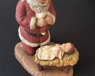 Santa Kneeling by Manger Figurine — Charming painted resin figurine showing Santa Claus kneeling beside a manger with the baby Jesus, perfect for Christmas display. The piece is painted in red, white, tan and gold tones with hand-painted detailing and a textured base; seller notes location: Office Up Room. Measures approximately 6.0 inches tall, 3.5 inches wide and 3.0 inches deep, a lightweight tabletop holiday accent. Good condition with minor paint wear consistent with age and use, no visible cracks or repairs. Ideal for seasonal mantel, shelf, or nativity grouping.