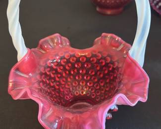 Fenton Cranberry Hobnail Basket — This charming Fenton cranberry hobnail basket features a distinctive twisted white milk glass handle and ruffled edge. The basket is crafted from rich cranberry glass with a textured hobnail pattern, a classic design hallmark of Fenton. It measures approximately 6 inches tall including the handle, with a 5-inch width across the top and 4 inches deep. The piece is in excellent condition with no chips or cracks visible, preserving its vintage charm. A perfect collectible for fans of Fenton glass or elegant vintage home decor.